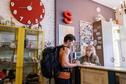 Administratoare de pensiune înregistrând la recepție sosirea unui turist cu rucsac