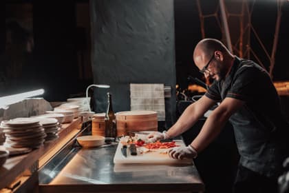Ajutor de bucătar tăind ardei pe un blat de inox, într-o bucătărie de restaurant