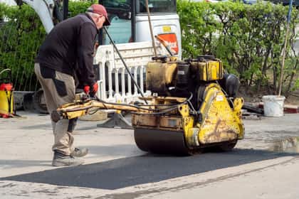 Asfaltator compactând cu un cilindru vibrator un petic de asfalt proaspăt așternut