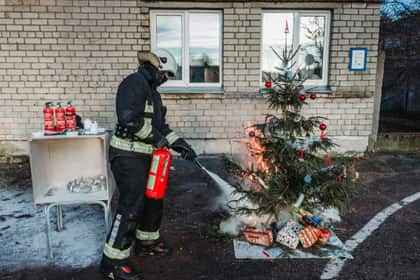 Demonstrație de stingere cu stingătorul a unui brad de Crăciun aprins, lângă o clădire