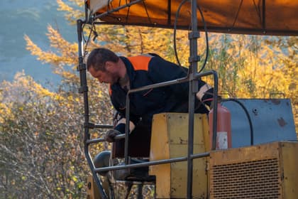 Muncitor la postul de comandă al unui repartizator-finisor de asfalt, pe un drum de munte
