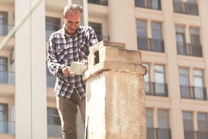 Un bărbat lucrează la coșul de fum de pe acoperișul unei case vechi, potrivind un tub la gura hornului.