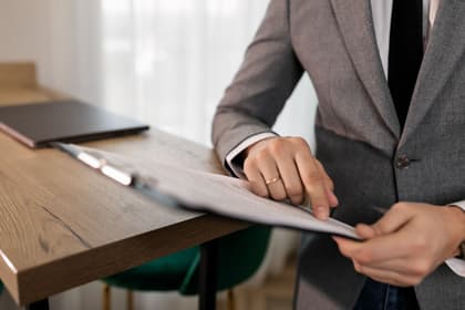 Expert în achiziții publice citind un document prins pe clipboard, la birou