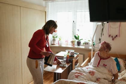 Infirmieră servind ceaiul unei paciente în vârstă, în salonul unui cămin