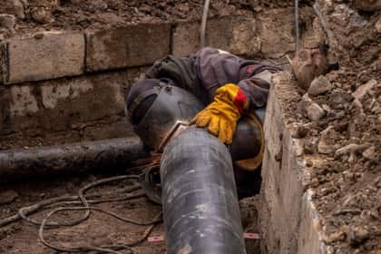 Instalator îmbinând o conductă într-un șanț săpat pe o stradă