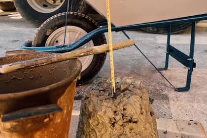 Măsurarea tasării betonului proaspăt pe șantier, cu o ruletă sprijinită pe conul de beton, lângă o găleată și o roabă.