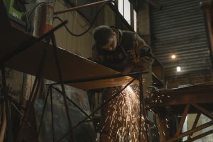 Lăcătuș lucrând la o structură din profile metalice, printre scântei, într-un atelier