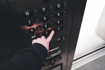 Mână apăsând butonul unui etaj pe panoul de comandă al unui lift