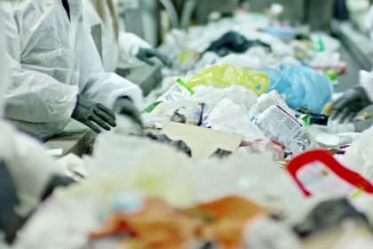 Lucrători în combinezoane albe și mănuși alegând deșeurile de pe banda unei stații de sortare