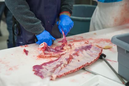 Măcelar dezosând o bucată de carne pe masa unei secții de tranșare