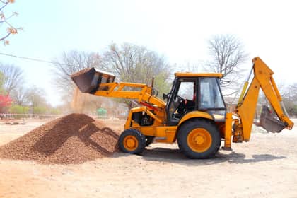Buldoexcavator galben descărcând pietriș pe un șantier