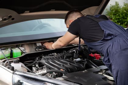 Mecanic auto aplecat peste motorul unei mașini cu capota ridicată