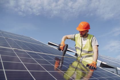 Montator cu cască și vestă reflectorizantă fixând cu mașina de înșurubat un panou solar