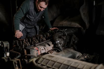 Motorist în salopetă lucrând la un motor diesel desfăcut