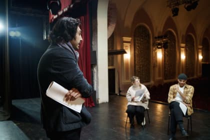 Organizator cu scenariul în mână coordonând o repetiție pe scena unui teatru