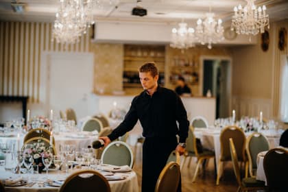 Ospătar turnând vin la mesele aranjate ale unei săli de restaurant