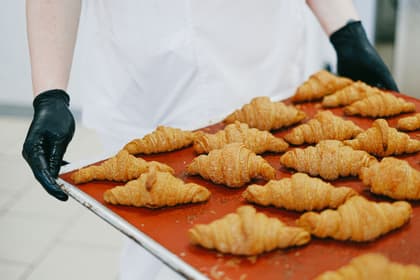 Patiser cu o tavă de croissante proaspăt coapte, într-un laborator de patiserie