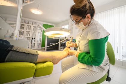 Pedichiuristă lucrând cu freza la piciorul unui client, într-un cabinet de pedichiură