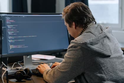 Programator scriind cod la un monitor mare, într-un birou