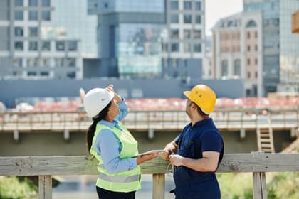Doi tehnicieni cu căști de protecție urmărind lucrările la un pod în construcție