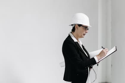 Tehnician cu cască de protecție notând pe o planșetă, într-o clădire în lucru