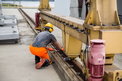 Tehnician de întreținere strângând cu cheia prinderile șinei de rulare a unui utilaj industrial