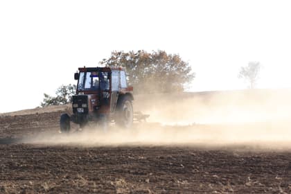 Tractorist lucrând pământul cu tractorul, într-un nor de praf